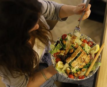 Overhead view of a woman eating a chicken salad balancing health with deliciousness.