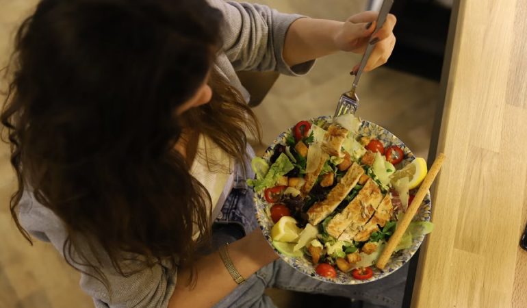 Overhead view of a woman eating a chicken salad balancing health with deliciousness.